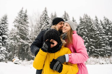 Mutlu aile kış ormanlarında eğlenir ve kameraya bakar. Anne, baba ve oğul karla oynuyor. Aile Noel konsepti. Birlikte vakit geçirmekten zevk alıyorum.