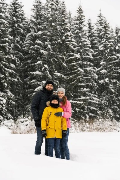 Mutlu aile kış ormanlarında eğlenir ve kameraya bakar. Anne, baba ve oğul karla oynuyor. Aile Noel konsepti. Birlikte vakit geçirmekten zevk alıyorum.