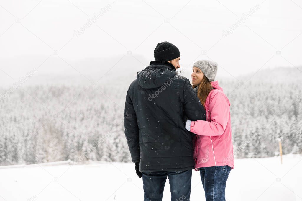 Loving couple in puffer jacket on a winter walk. Man and woman posing in the frosty forest. Romantic date in winter time.Christmas mood of a young family.Winter lovestory