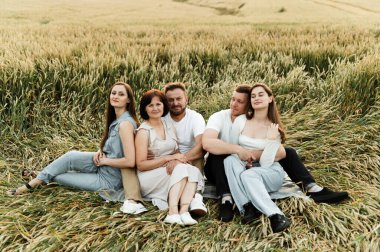 Bir çiftçi ailesi gün batımında buğday tarlasında oturur ve sevinir, organik hasat, eko buğday bir aile tarafından yetiştirilir, beş kişilik bir aile bir tarlada dinlenir.