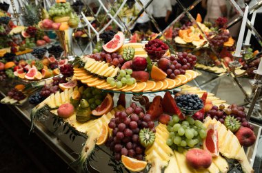Üzerinde çeşitli egzotik meyve ve şekerlerin olduğu düğün meyve masası. Meyveli çikolata. Ziyafette armut, elma, ananas ve daha bir sürü yiyecek.