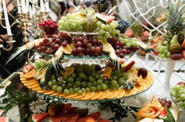 Üzerinde çeşitli egzotik meyve ve şekerlerin olduğu düğün meyve masası. Meyveli çikolata. Ziyafette armut, elma, ananas ve daha bir sürü yiyecek.