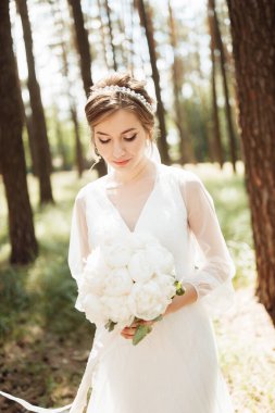 Ormanda zarif bir gelin duruyor ve elinde şakayıkla güzel bir düğün buketi tutuyor.