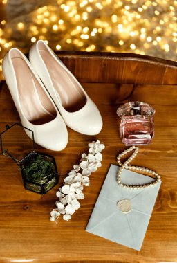 Düğün sabahı. Gelin aksesuarlarının güzel kompozisyonu. Yosun dolu bir kutuda yüzükler, güzel bir zarf, dekorasyon. Aksesuarlar ahşap bir masanın üzerinde, çelenklerin arka planında yatıyor.