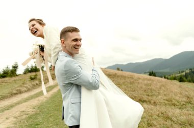 Neşeli damat kollarında güzel bir gelin tutuyor. Mutlu genç çift düğün günü eğleniyor ve şımartıyor.