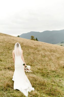 Beyaz elbiseli güzel bir gelin ve bir buket kurumuş çiçekle sonbahar dağlarında sarı otların arasında.