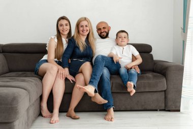 Neşeli aile evdeki kanepede oturuyor. Kel ve sakallı bir baba karısına ve çocuklarına sarılıyor. Aile kavramı. Aile eğlencesi