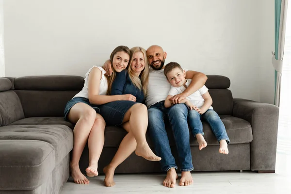 Neşeli aile evdeki kanepede oturuyor. Kel ve sakallı bir baba karısına ve çocuklarına sarılıyor. Aile kavramı. Aile eğlencesi