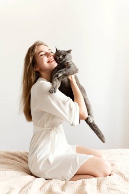 İnce pijamalı seksi bir kız yatağa oturur ve güzel bir İskoç kedisi tutar. Evde pijamalı, evcil bir hayvanla yatakta seksi bir kız.