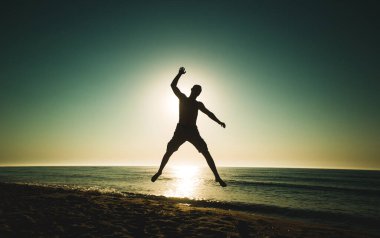 Okyanusun üzerinde güneşin doğuşunun arka planında atlayan bir adamın silüeti. Sporcu silueti. saglikli yasam tarzi