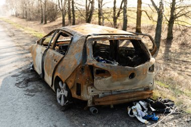 Ukrayna 'daki savaştan kalma yanmış bir araba. Yoldaki araba kazası. Yolun kenarında yanmış bir araba var. arızalı ulaşım.