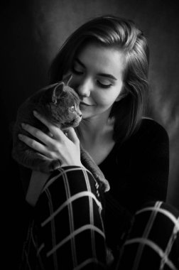 Pijamalı güzel bir kız sandalyede oturur ve İskoç bir kediye sevgiyle sarılır. Evcil bir kediye sarılan sevimli ve gülümseyen bir kız. yerli gri İngiliz kedisi.