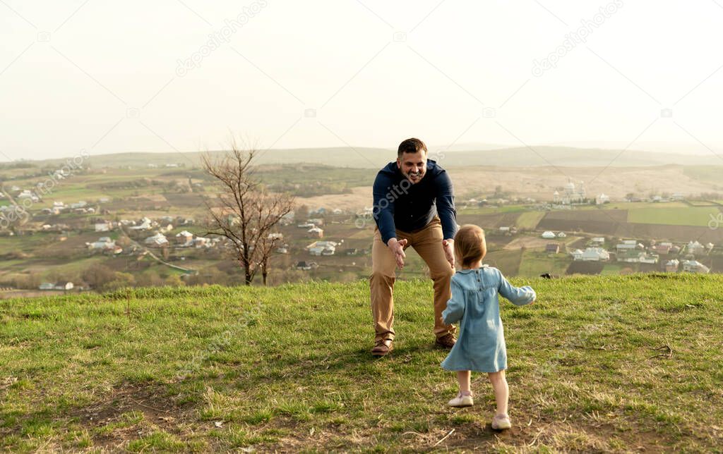 Father throws up and spins his daughter in nature in springtime. Dad and girl play in the park at sunset. The girl is flying. Friendly family concept. Close-up