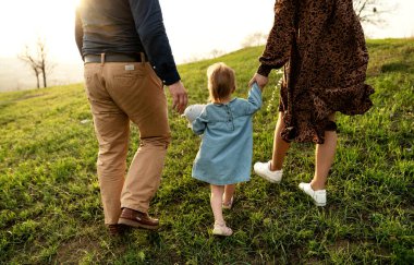 Mutlu aile bahar çimlerinde yürüyor. Küçük kızı ve kocası olan hamile bir kadın. Aile gün batımında yürür. Uluslararası aile. Gelecekteki ebeveynler. hamile karnı