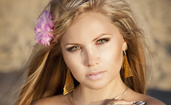 Mujer rubia seductora con flores en el pelo y joyas de oro posando — Foto de Stock