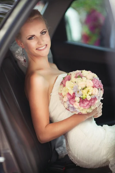Счастливая невеста в машине с свадебным букетом — стоковое фото