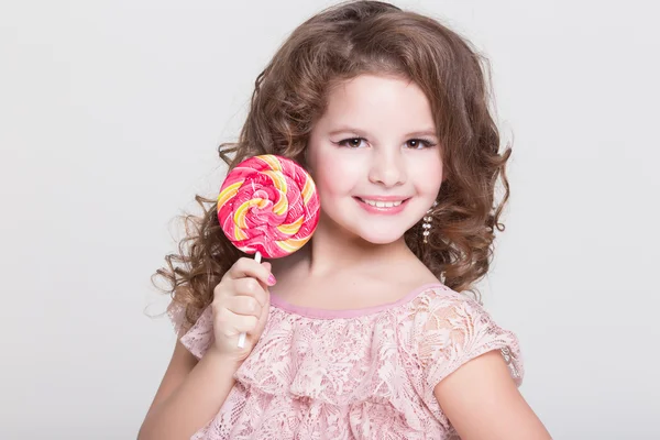 Morsomt barn med godteri kjærlighet på pinne, glad liten jente som spiser stor sukkerbit, barn som spiser godteri. overrasket barn med godteri . – stockfoto