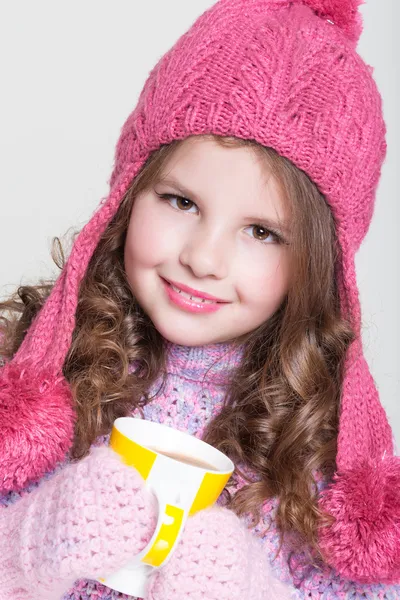 Mooi kind in winter hoed drinken warme chocolade, weinig meisje in wollen accessoires met kopje thee of cacao. — Stockfoto