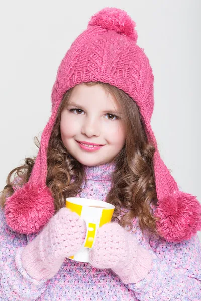 Mooi kind in winter hoed drinken warme chocolade, weinig meisje in wollen accessoires met kopje thee of cacao. — Stockfoto