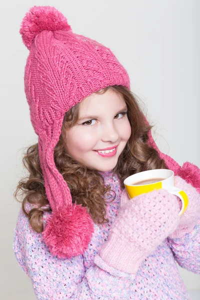 Mooi kind in winter hoed drinken warme chocolade, weinig meisje in wollen accessoires met kopje thee of cacao. — Stockfoto
