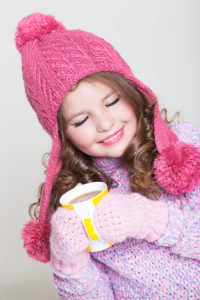 Mooi kind in winter hoed drinken warme chocolade, weinig meisje in wollen accessoires met kopje thee of cacao. — Stockfoto