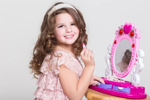Χαριτωμένο μικρό κορίτσι με το παιχνίδι του καθρέφτη και κραγιόν. — Φωτογραφία Αρχείου
