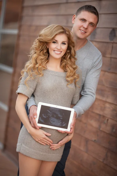 Pregnant woman with husband holding ultrasound scan on her tummy — Stock Photo, Image