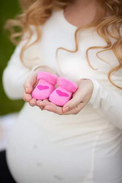 Pregnant woman belly holding pink baby booties — Stock Photo, Image