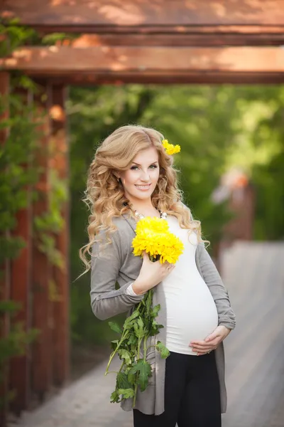 Glad gravid kvinna utomhus med vårblommor i grön park — Stockfoto