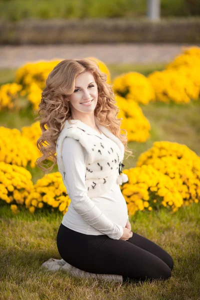 Happy pregnant woman outdoors with spring flowers in green park — Stock Photo, Image