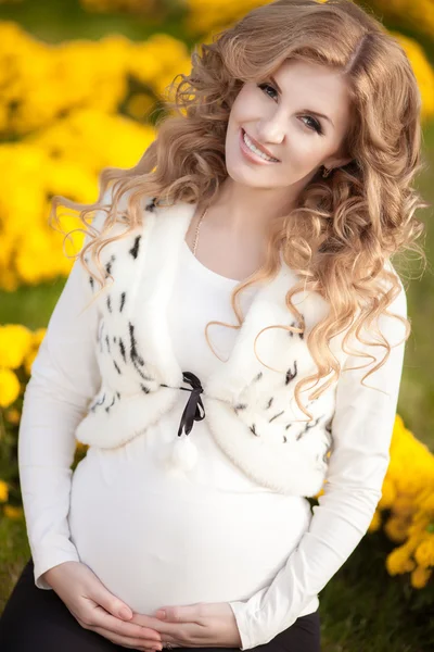 Happy pregnant woman outdoors with spring flowers in green park — Stock Photo, Image