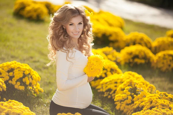 Heureuse femme enceinte en plein air avec des fleurs de printemps dans un parc vert — Photo