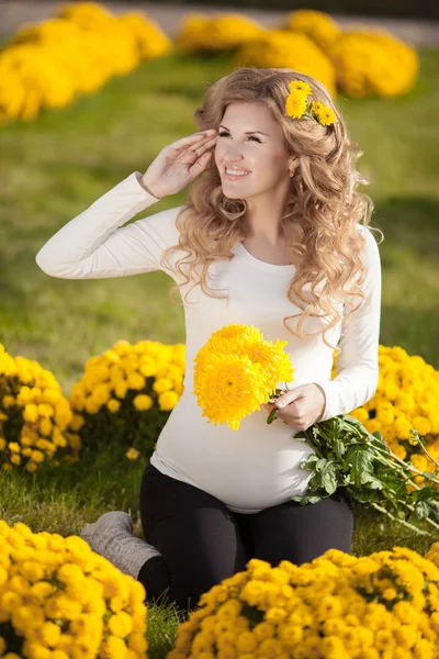 Mujer embarazada feliz al aire libre con flores de primavera en el parque verde —  Fotos de Stock