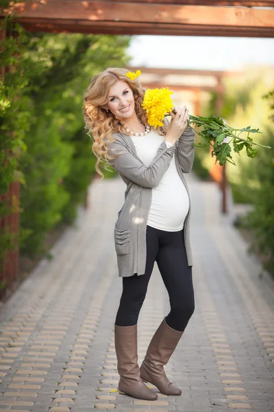 Glad gravid kvinna utomhus med vårblommor i grön park — Stockfoto