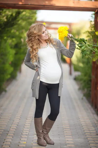 Ευτυχισμένη έγκυος γυναίκα σε εξωτερικούς χώρους με ανοιξιάτικα λουλούδια σε καταπράσινο πάρκο Εικόνα Αρχείου