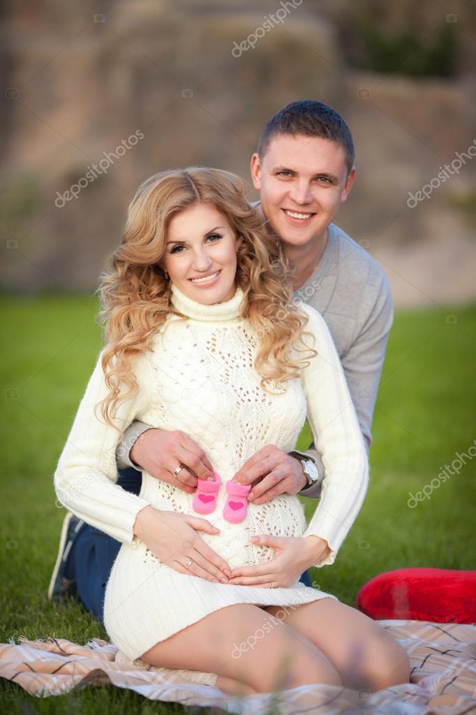 Pregnant woman and her husband relaxing on nature and have picnic in park