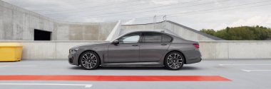 Lüks gri BMW 740D, G12 model, boş bir otoparka park edilmiş. Bulutlu bir gün. Başka araba ve insanlar yok. Katowice, Polonya, 12.06.2021