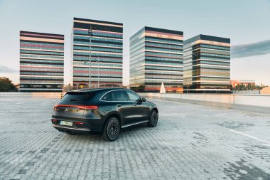Gün batımında otoparkta elektrikli Mercedes EQC spor SUV. Arka planda modern ofis binaları. Arabanın gücü 408km. 'dir. Menzil (WLTP) 369-414 km. Katowice, Polonya, 10 Haziran 2020
