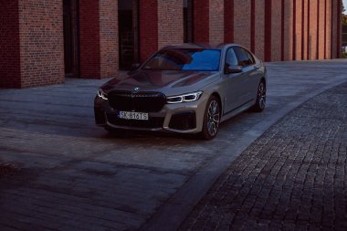 Gri BMW 740D xDrive NOSPR konser salonunun önünde. Araba batan güneşin ışınlarıyla aydınlanır. 340 HP motoru, hız 0-100 km / saat - 5s Katowice, Polonya, 12.06.2021