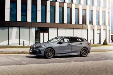 Gri BMW 1 M Sport versiyonu, modern bir ofis binasının önüne park edilmiş. Başka araba ve insanlar yok. Katowice, Polonya, 18.07.2020