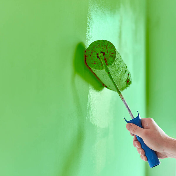 Close-up on the hand of a man who is painting a wall green with a paint roller.  Painting apartment, renovating with green color paint.