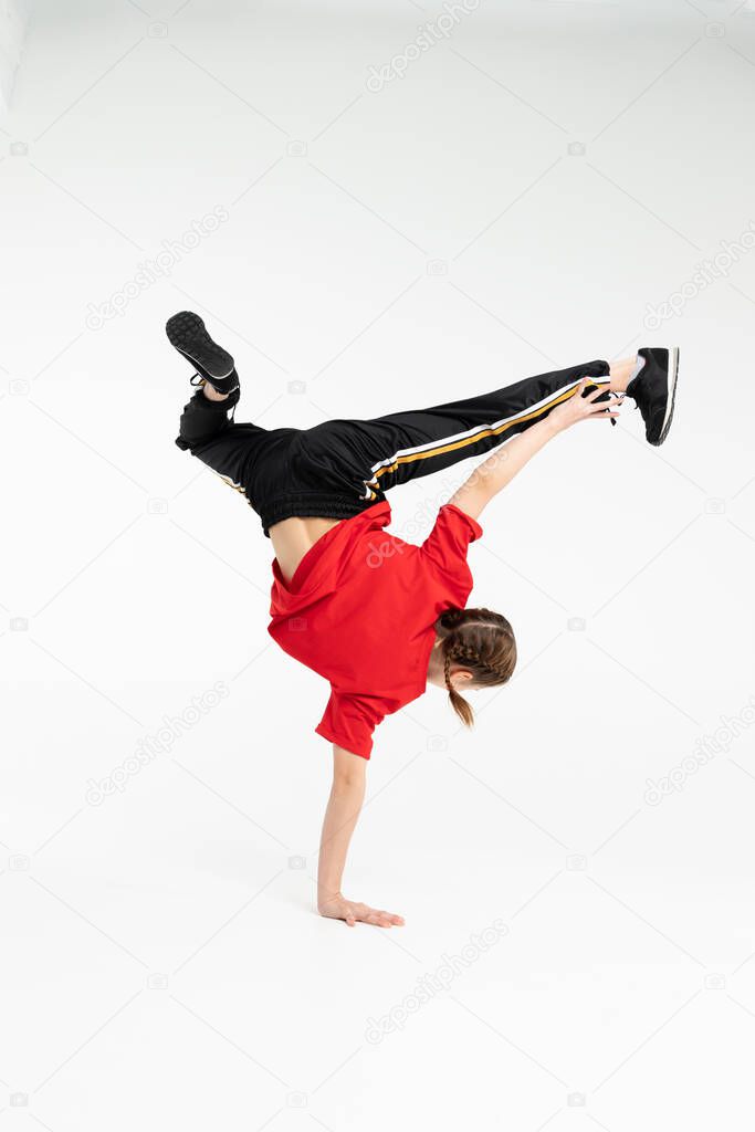 Isolated young Russian girl hip hop break dancer dancing in grey studio background, performing freeze of downrock breakdance