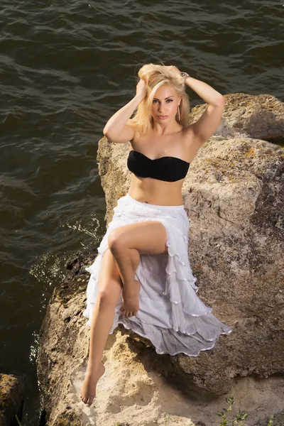 Piękna blondynka z długimi włosami na skały i morze — Zdjęcie stockowe
