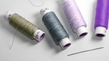 Rolls with threads of various colors and one needle on the white background