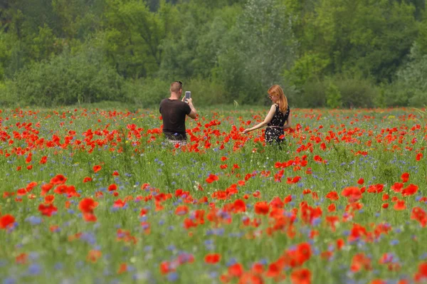 The guy with the girl are photographed in a field of red poppies.