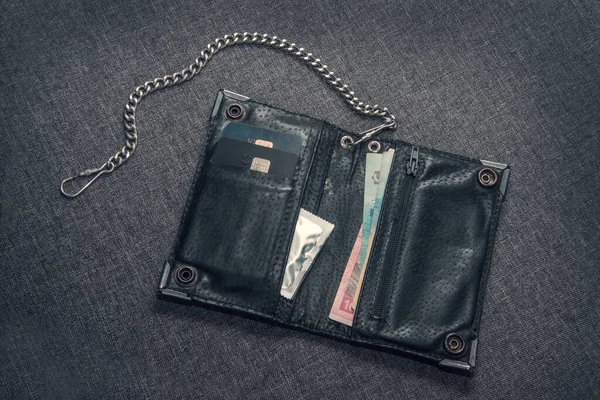 Men\'s black leather wallet on the chain. There are payment cards, money and condoms in the wallet.