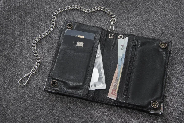 Men\'s black leather wallet on the chain. There are payment cards, money and condoms in the wallet.