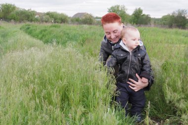 Woman with short red hair. Woman with a small son among tall grass. Woman with a small child walk along the meadows.