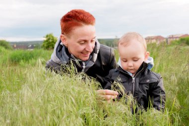 Woman with a small son among tall grass. Woman with a small child walk along the meadows. Woman with short red hair. 