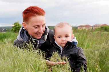 Woman with a small son among tall grass. Woman with a small child walk along the meadows. Woman with short red hair. 